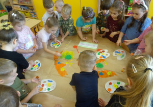 Grupa dzieci stempluje pomponami maczanymi w farbie sylwetę motyla.